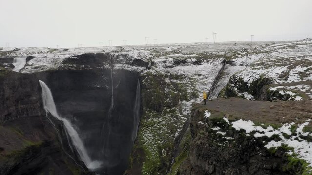Aerial: One person wearing yellow jacket, looking at Granni waterfall in Iceland