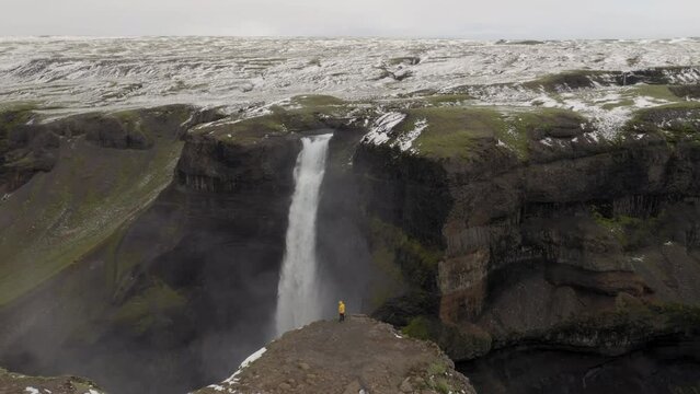 Aerial: One man with yellow jacket, standing near the edge of a cliff near Haifoss waterfall in Iceland