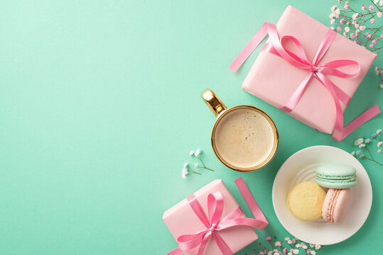 Spring concept. Top view photo of pink gift boxes with ribbon bows plate with macarons cup of fresh coffee and gypsophila flowers on isolated turquoise background with copyspace
