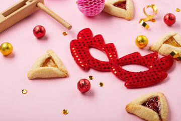 Hamantaschen Cookies, Red Carnival Mask, Noisemaker on Pink Background. Purim Celebration, Jewish Carnival Holiday Concept.