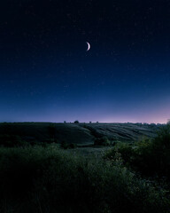 Crescent Moon in starry night sky over hills. A fabulous night landscape.