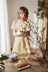 A teenage girl decorates the branches of the house with Easter eggs. Easter decoration for the holiday