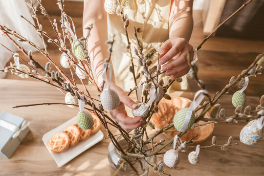 Close-up of a girl's hands hanging a decorative Easter egg on a willow branch at home. Decorating your home for Easter