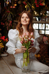 A young female florist in white clothes works in an authentic flower shop, making bouquets in a flower shop. Workplace of a flower shop employee.
