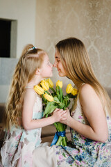 Mother's day concept. Girl congratulates mother and gives a bouquet of yellow flowers tulips at home. Mom and daughter smiling and hugging. Holiday greeting card for International Women's Day. Closeup
