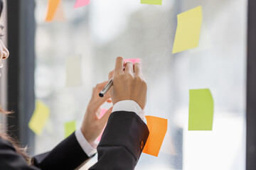 Business female employee with many conflicting priorities arranging sticky notes commenting and brainstorming on work priorities colleague in a modern office.

