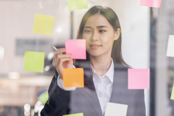 Business female employee with many conflicting priorities arranging sticky notes commenting and brainstorming on work priorities colleague in a modern office.
 - obrazy, fototapety, plakaty