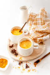 Goldene Milch mit Kurkuma in zwei Tassen auf einem Holz Serviertablett. Weißer Tisch.