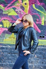A woman with leather clothes on the background of a wall with graffiti