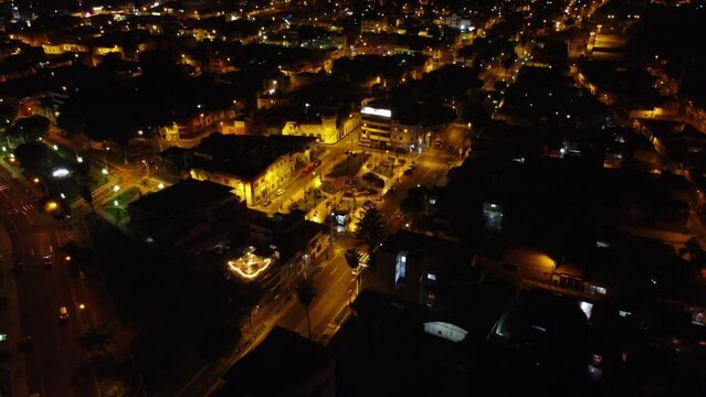 Night time lights shine through a city as drone flies backwards and upwards revealing the entirety of the city with lights going on into the horizon. Located in Chorrillos district of Lima, Peru.