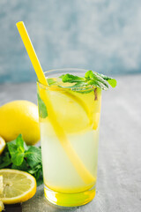 Lemonade drink or mojito cocktail in a glass with straw, lemon fruit and mint leaves, refreshing summer beverage