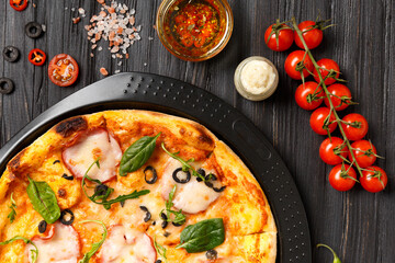 Pizza on a black dish on a dark wooden background top view.