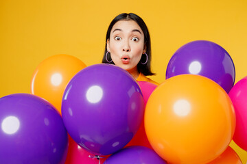 Fototapeta na wymiar Close up excited shocked impressed pop-eyed fun young woman wearing casual clothes celebrating behind bunch of balloons isolated on plain yellow wall background. Birthday 8 14 holiday party concept.