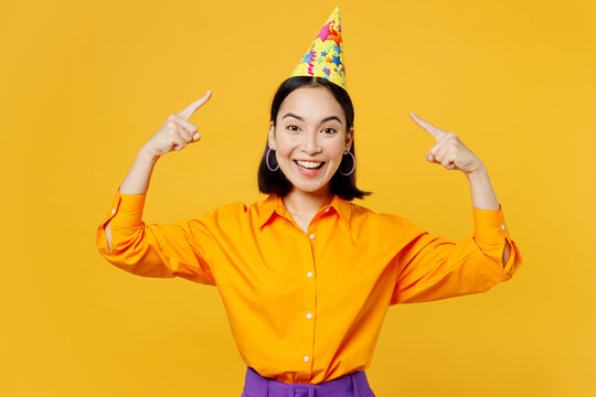 Happy smiling cheerful excited positive joyful fun young woman wearing casual clothes pointing index finger on hat celebrating isolated on plain yellow background. Birthday 8 14 holiday party concept.