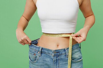 Cropped young woman in white clothes show loose pants after weightloss hold measure tape on waist...