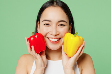 Close up young happy woman in white clothes hold in hand yellow red bell pepper look camera isolated on plain pastel light green background Proper nutrition healthy fast food unhealthy choice concept.