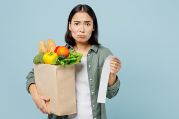 Young shocked sad woman wearing casual clothes hold brown paper bag with food products look at...
