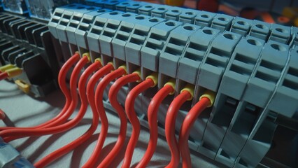 Gray plastic electrical panel with many red wires, yellow bushing ferrules screwed to the panel, electrical parts, automatic switches, breakers. Close up of a high voltage electrical switch.