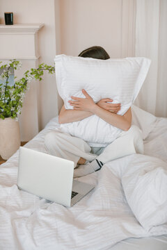 Woman sitting in bed in front of her laptop computer cuddling a pillow