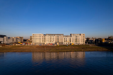 Fototapeta premium Luxury residential Kade Zuid apartment complex construction at riverbank of river IJssel reflecting in the water contrasted against a clear blue sky