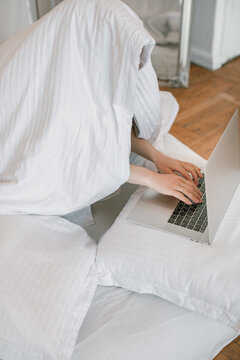 Woman sitting in bed wrapped in a duvet working on her laptop computer