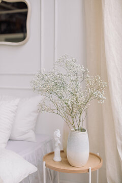 Vase of white gypsophila flowers on a side table next to a bed