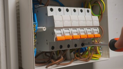 Electrician assembles electrical panel. Close up of a man hands tightening screw with a screwdriver...