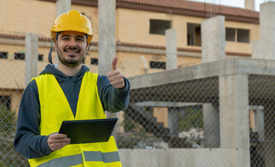 Retrato de operario de obra, con expresión feliz, alzando el dedo pulgar , con la Tablet en un edifico en construcción.
