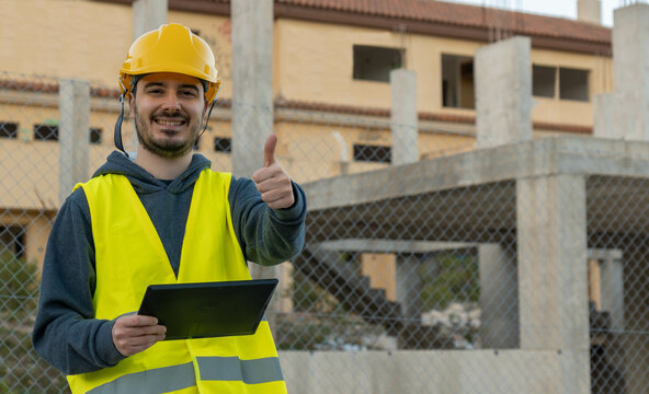 Retrato de operario de obra, con expresi&oacute;n feliz, alzando el dedo pulgar , con la Tablet en un edifico en construcci&oacute;n.