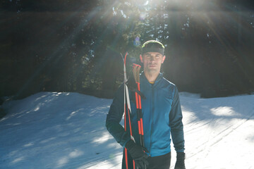 Portrait handsome male athlete with cross country skis in hands and goggles, training in snowy...