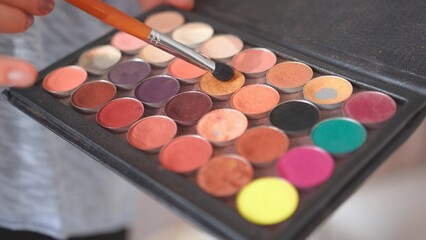 Makeup artist holds shadows in his hand and paints a model.