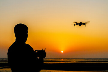Silhouette of a drone pilot operating a drone standing by the sea at evening sunset. Silhouette view of a drone pilot. © Onuchcha