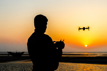 Silhouette of a drone pilot operating a drone standing by the sea at evening sunset. Silhouette view of a drone pilot.