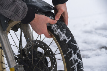 checks the pressure The motorcycle wheel is close-up. Rubber and tread are clogged with snow....