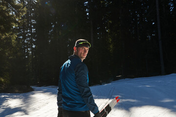 Portrait handsome male athlete with cross country skis in hands and goggles, training in snowy...