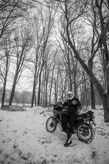 Motorcyclists enjoy extreme winter riding on a motorcycle, snowy forest, snowfall. The concept of transport and clothing for the cold season. Stupid ideas of grown men. Vertical photo. Black and white