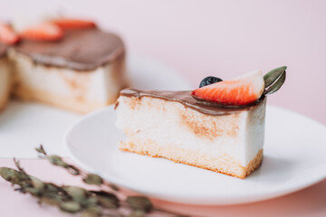Bird's milk cake with chocolate decorated with strawberries and grapes with piece on white plate on pink background.