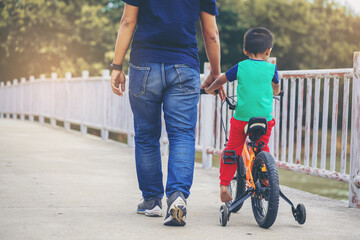 Asian father training his son learn to ride a bicycle at outdoor park.
