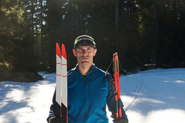Portrait handsome male athlete with cross country skis in hands and goggles, training in snowy...
