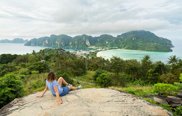 Woman sitting on the viewpoint, in the background the two bays of the island of phi phi don in...