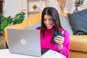 Smiling ethnic woman with cup of coffee using laptop