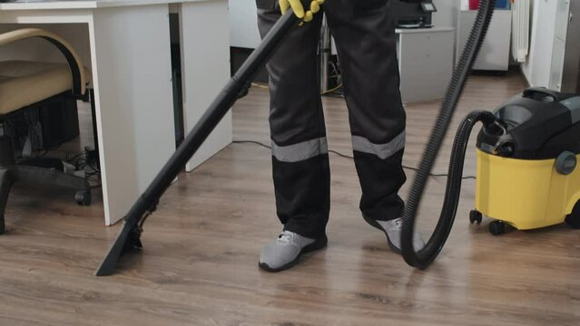 Slow motion shot of young African American professional cleaning worker wearing uniform using vacuum cleaner to get rid of dust on floor in office