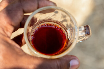 Cup of red raw tea held in fingers. Red tea and its bubbles are seen from above. Holding tea cup on fingers.