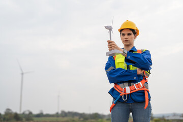 Female engineer in uniform and helmet safety holding wind turbine model. Technician woman inspector working in wind turbine farm to generate electrical energy, Renewable power energy.