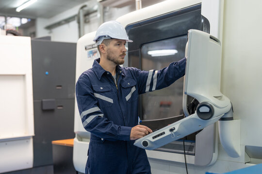 Male engineer using computer control panel cnc machine operating at factory. Man technician in uniform and helmet safety working at workshop heavy metal industrial