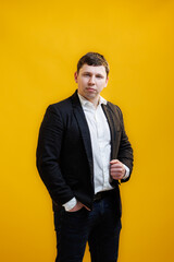 Fototapeta premium Portrait of focused businessman wearing suit standing on yellow studio background and looking at camera