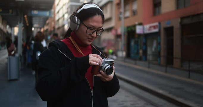 Young asian street photographer using analogic 35 mm photo camera outdoor with city in background