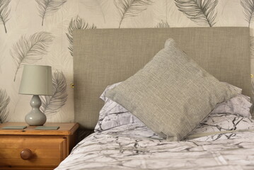 interior of a bedroom with a cushion, bedside table, and table lamp, flower wallpaper