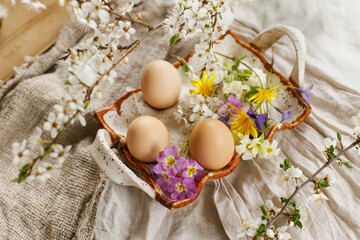 Happy Easter! Rustic easter still life. Stylish easter eggs and blooming spring flowers on linen fabric background. Natural eggs in tray and wildflowers