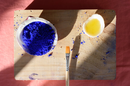 Pigmento azul cobalto en una concha, aceite en otra concha y pincel sobre madera, que a su vez est&aacute; colocada sobre una tela cobriza, y todo ello recibiendo la proyecci&oacute;n de luces y sombras. 